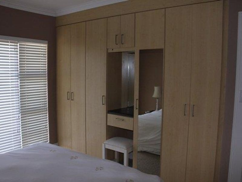 Bedroom featuring extensive light wood built-in cupboards with an integrated vanity area and venetian blinds.
