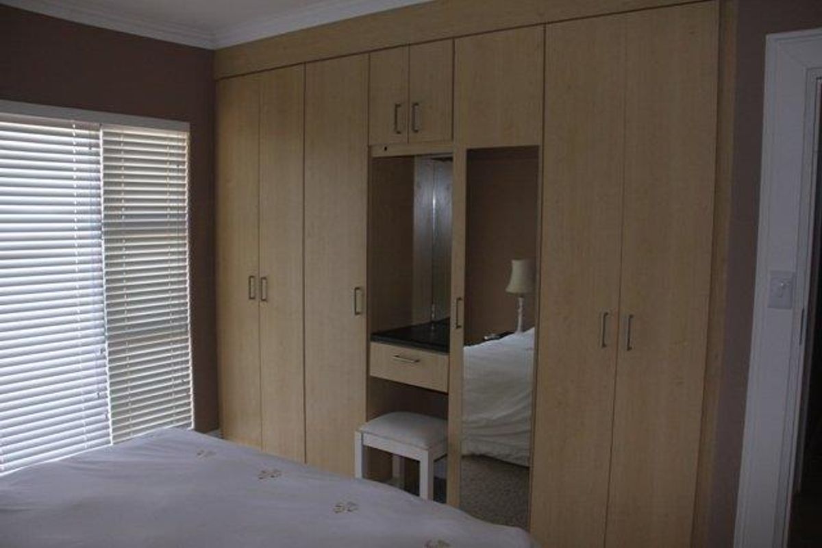 Bedroom featuring extensive light wood built-in cupboards with an integrated vanity area and venetian blinds.