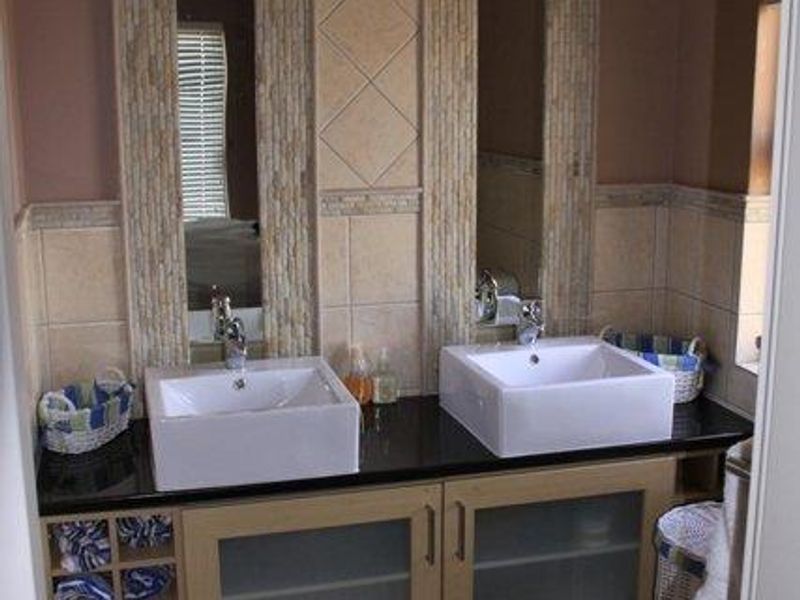 A modern bathroom featuring a double vanity with vessel sinks, granite countertops, and decorative tiled wall accents with integrated mirror panels.