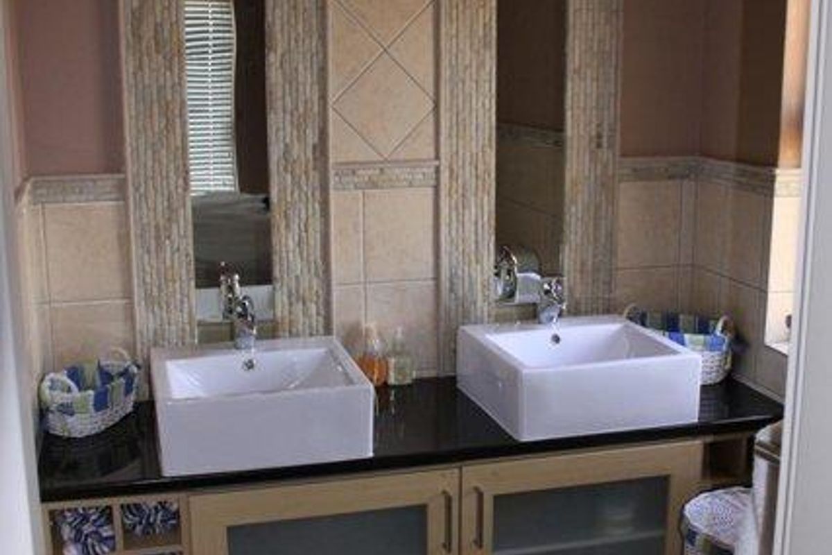 A modern bathroom featuring a double vanity with vessel sinks, granite countertops, and decorative tiled wall accents with integrated mirror panels.