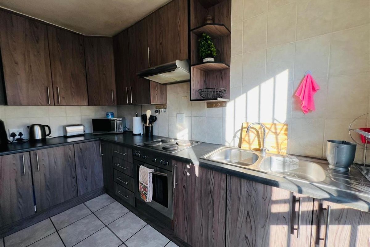 A functional kitchen featuring dark wood-grain cabinetry, a built-in oven with extractor fan, double stainless steel sink, and tiled flooring.