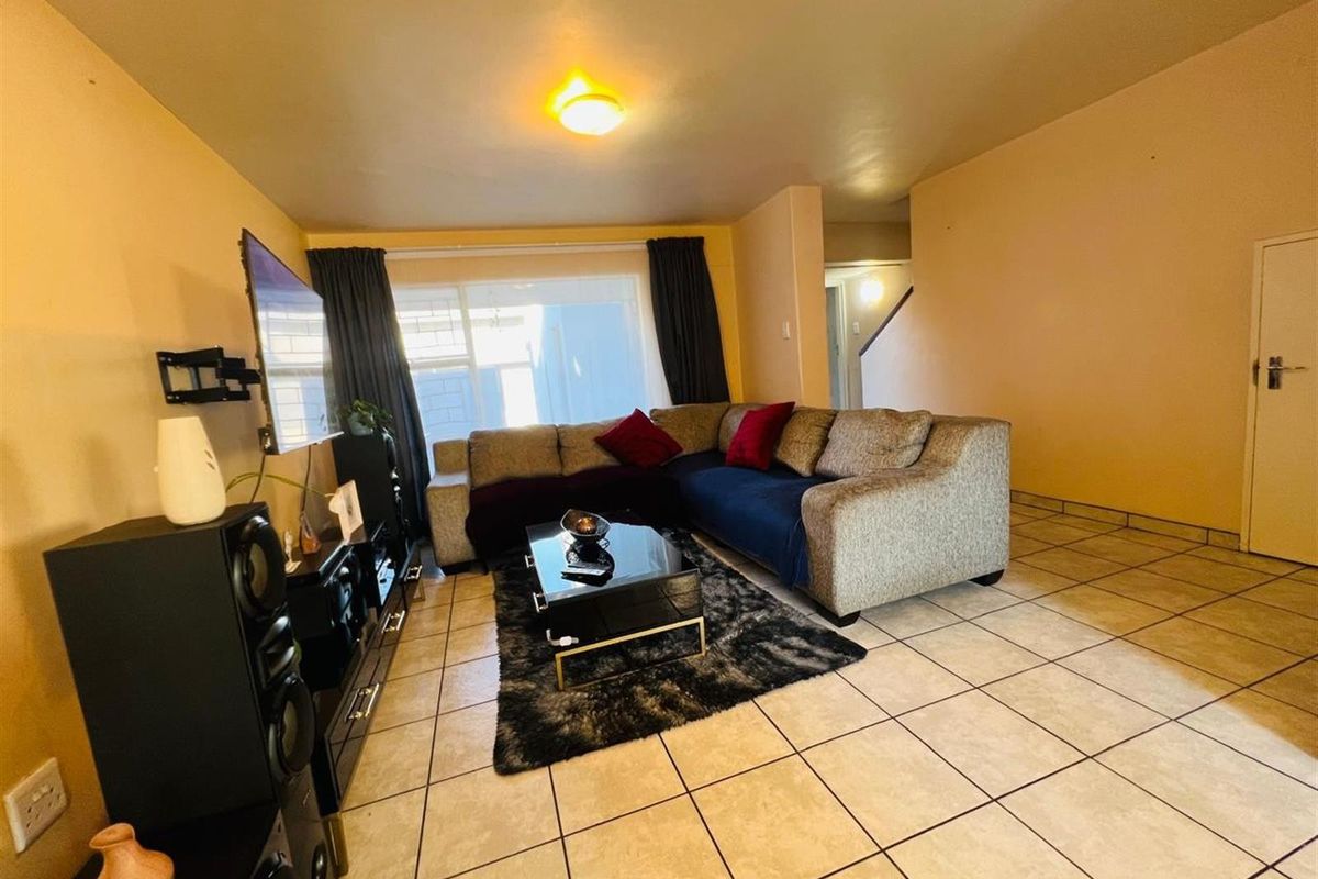 A spacious living room featuring neutral floor tiles, large window for natural light, and a functional layout suitable for comfortable family living.