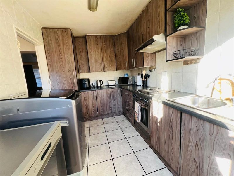 A functional kitchen featuring wood-grain cabinetry, built-in oven, extractor fan, and tiled flooring with ample counter space for meal preparation.