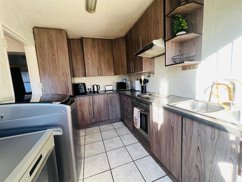 A functional kitchen featuring wood-grain cabinetry, built-in oven, extractor fan, and tiled flooring with ample counter space.