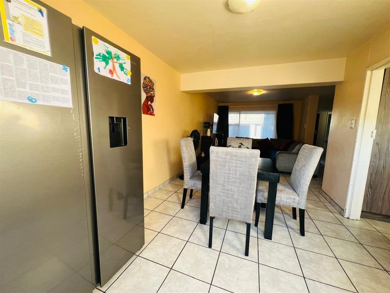 An open-plan living and dining area featuring tiled flooring, neutral wall tones, and a functional layout connecting the kitchen space to the lounge.
