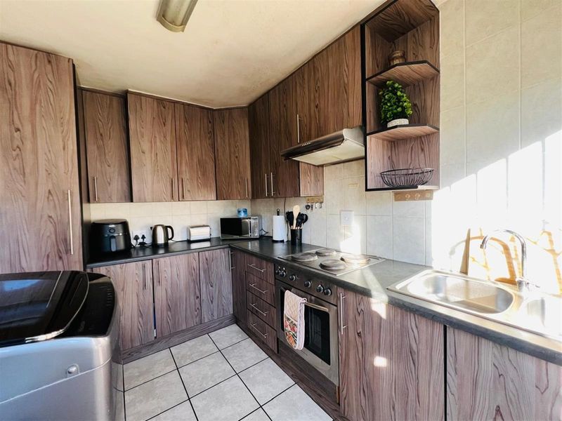 A functional kitchen featuring wood-grain cabinetry, a built-in oven with hob, extractor fan, and tiled flooring with a stainless steel sink.