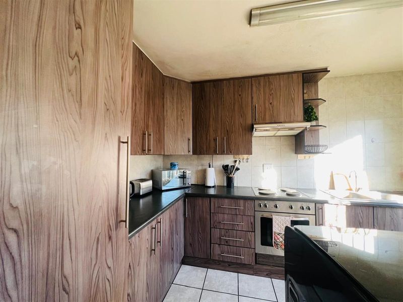 Functional kitchen featuring wood-grain cabinetry, dark countertops, built-in oven, extractor fan, and tiled flooring.
