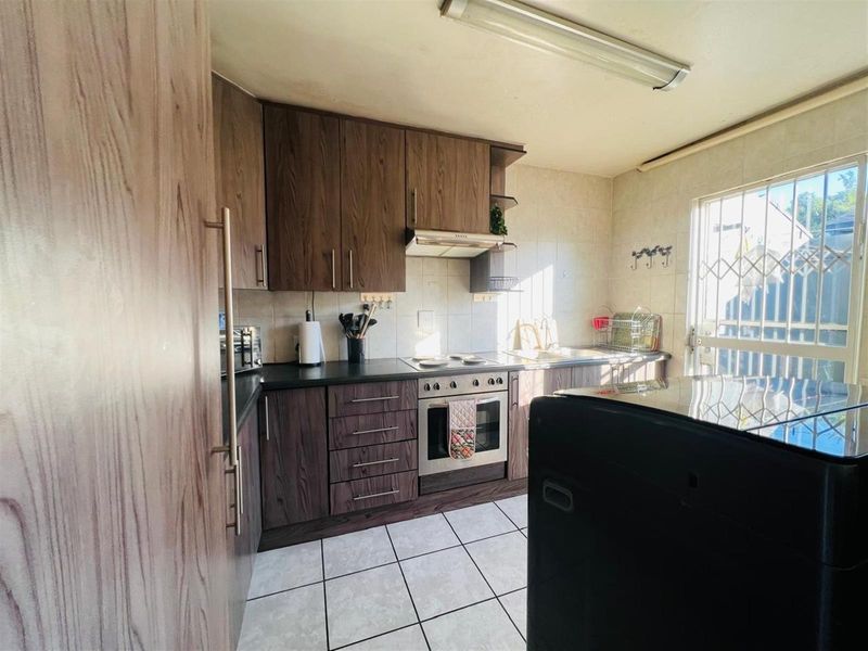 A functional kitchen featuring wood-grain cabinetry, a built-in oven with extractor fan, tiled splashbacks, and direct access to an exterior security gate.