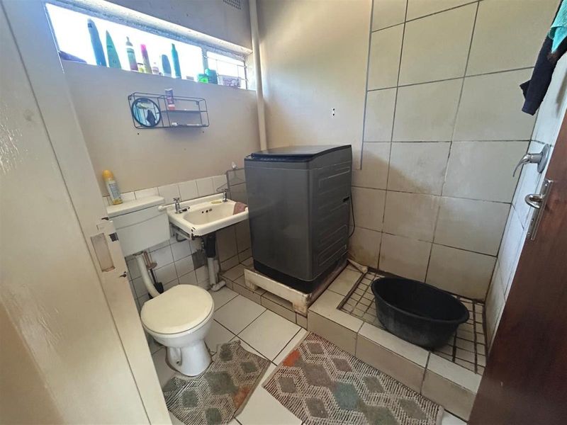 A functional laundry area featuring a toilet, wall-mounted basin, and tiled finishes, requiring maintenance and cosmetic updates.