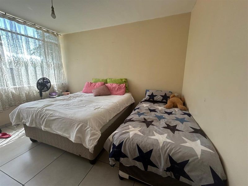 A bedroom featuring tiled flooring and a large window, currently configured with two beds.