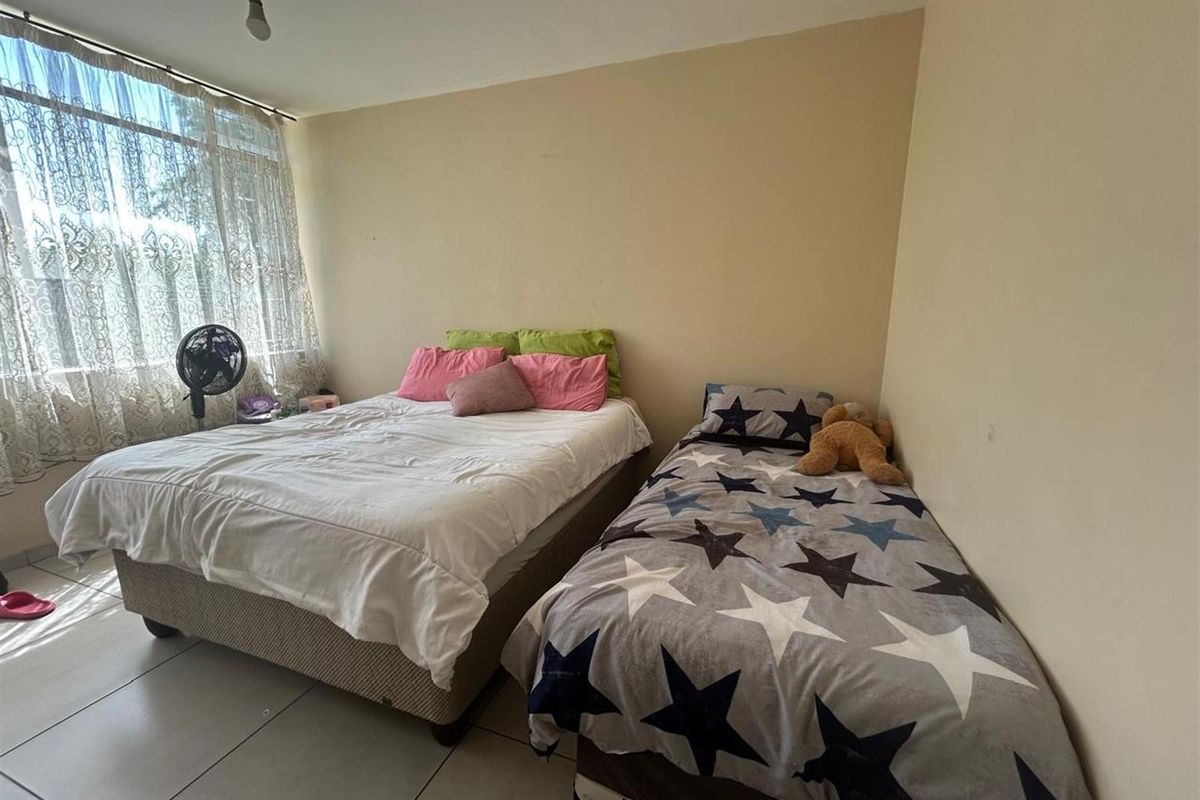 A bedroom featuring tiled flooring and a large window, currently configured with two beds.