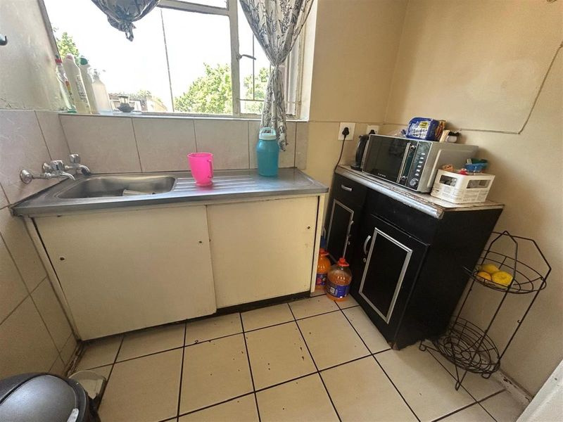 A compact kitchen area featuring a stainless steel sink, tiled splashback, and built-in cabinetry with tiled flooring.