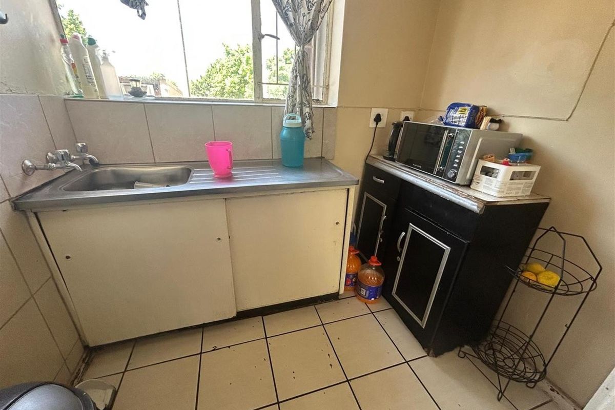 A compact kitchen area featuring a stainless steel sink, tiled splashback, and built-in cabinetry with tiled flooring.