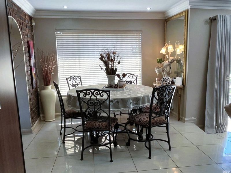 A well-maintained dining room featuring tiled flooring, an exposed brick feature wall, recessed lighting, and crown molding.