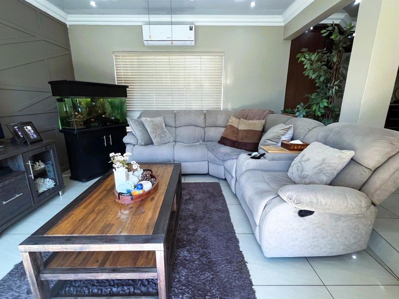 A comfortable living room featuring tiled flooring, cove ceiling molding, and a wall-mounted split-system air conditioner.