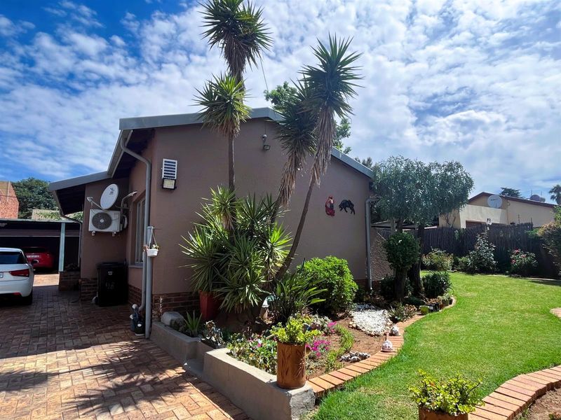 Rear exterior view of the property featuring a brick paved driveway, landscaped garden beds, and a well-maintained lawn area.
