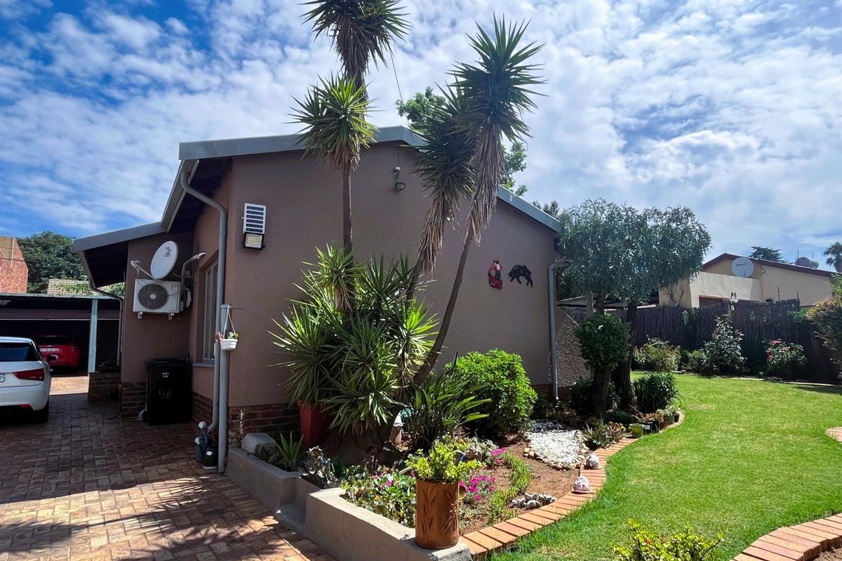Rear exterior view of the property featuring a brick paved driveway, landscaped garden beds, and a well-maintained lawn area.