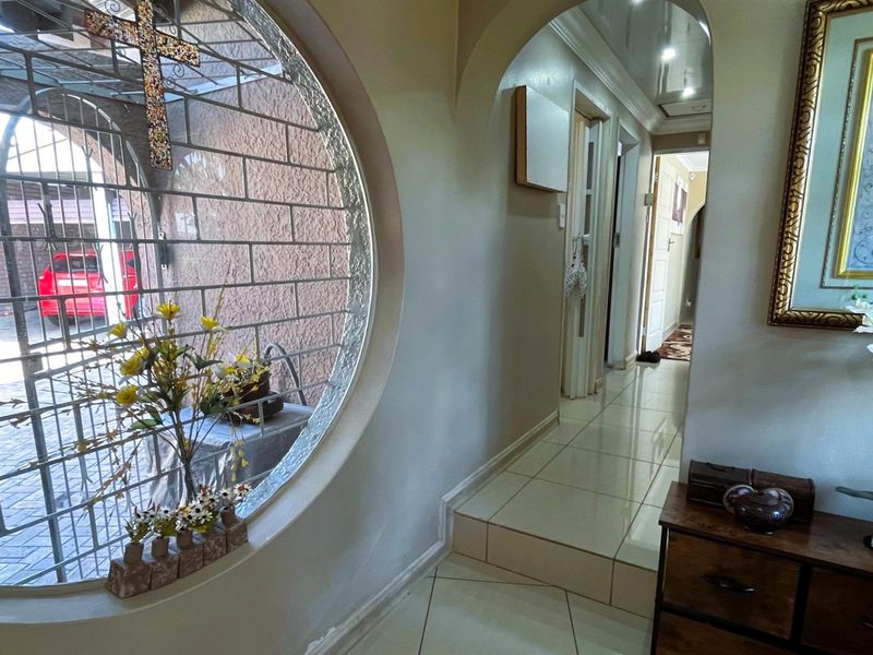 A bright hallway featuring a unique circular window, tiled flooring, and an arched transition leading into the interior living spaces.