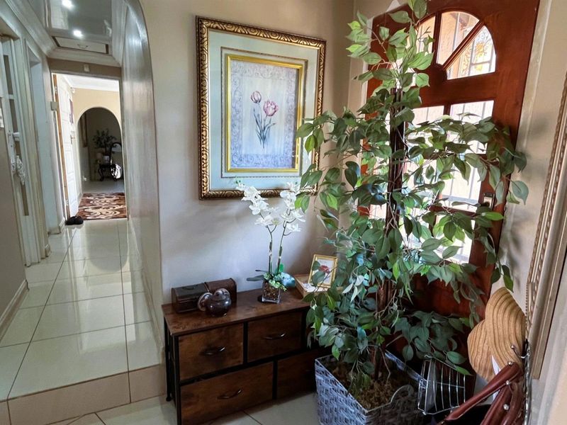 A welcoming entrance hall featuring polished tiled flooring, an arched transition to the hallway, and a classic timber front door with decorative glass.