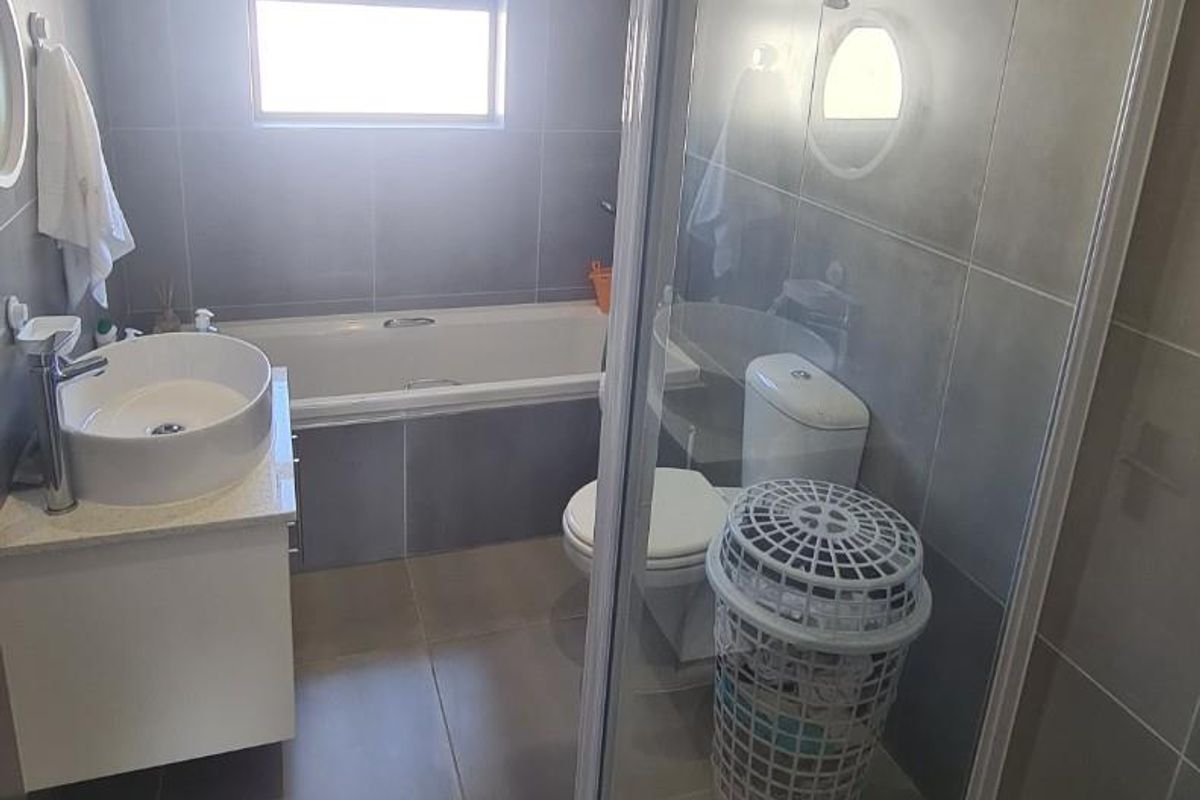 Modern bathroom featuring a glass-enclosed shower, a separate bathtub, a vanity basin, and neutral floor-to-ceiling tiling.