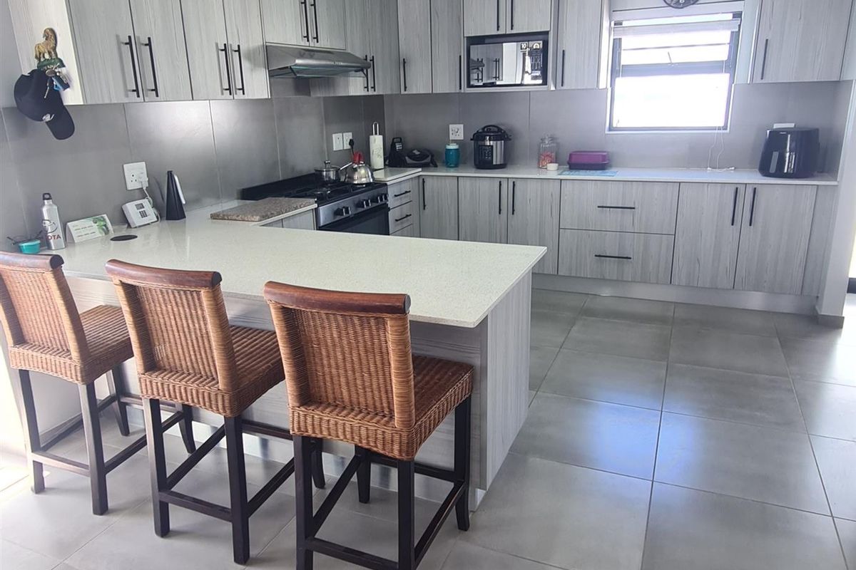Modern kitchen featuring light wood-grain cabinetry, stone countertops, a breakfast bar, and integrated stainless steel appliances including a gas hob and extractor fan.
