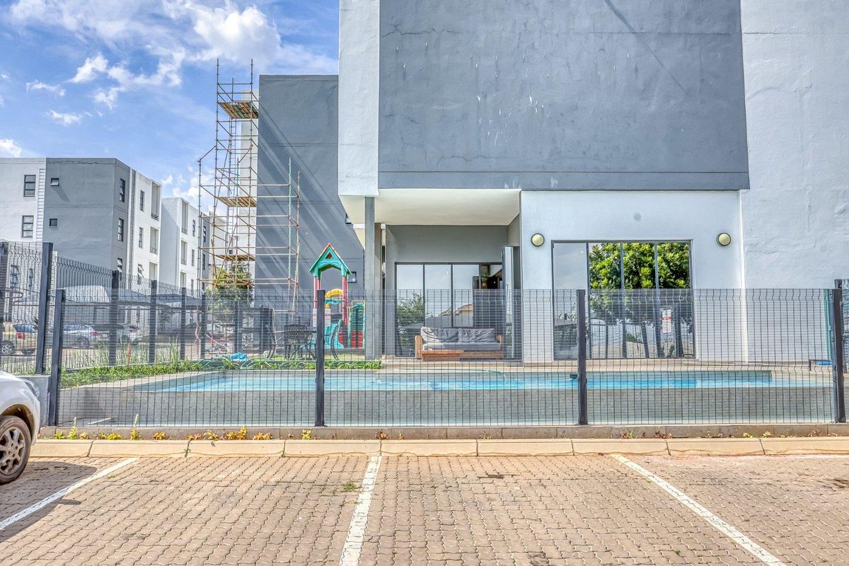 Exterior view of an apartment unit featuring a private swimming pool, paved parking area, and a covered patio space.