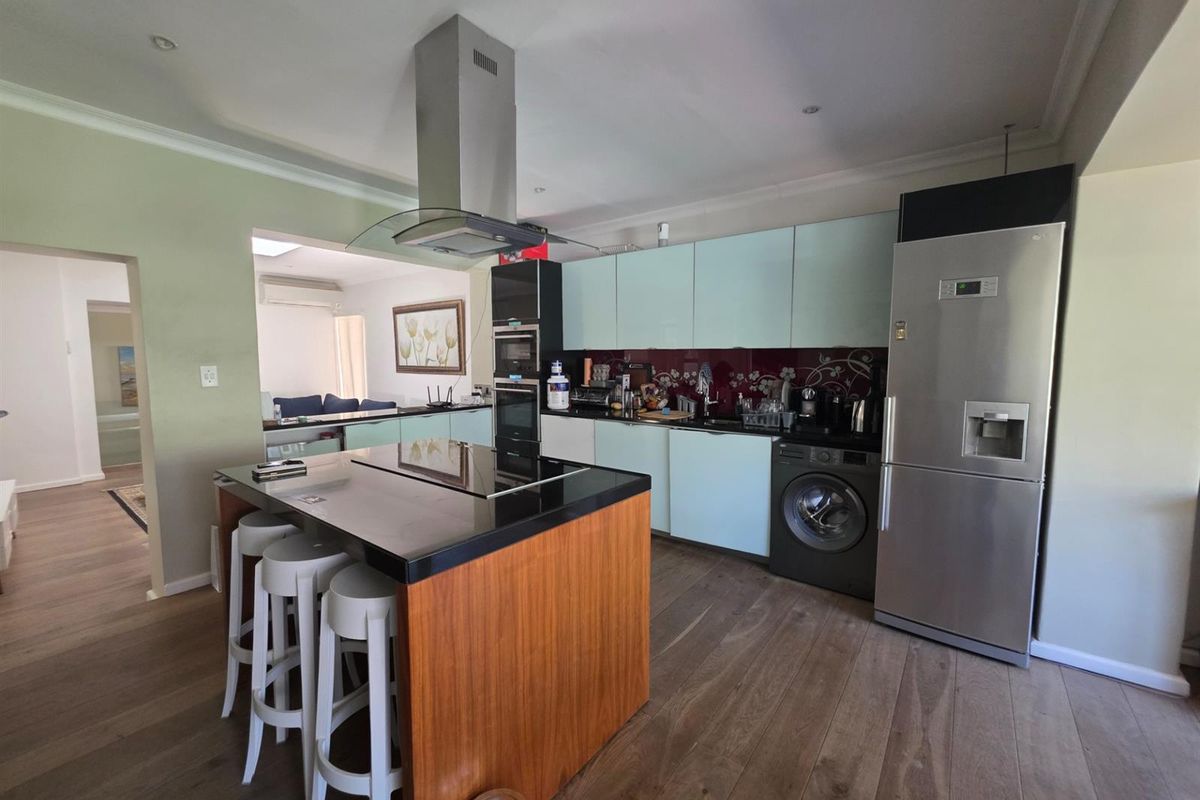 Modern kitchen featuring a central island with hob, integrated cabinetry, built-in appliances, and sleek finishes, seamlessly flowing into the adjacent living area.