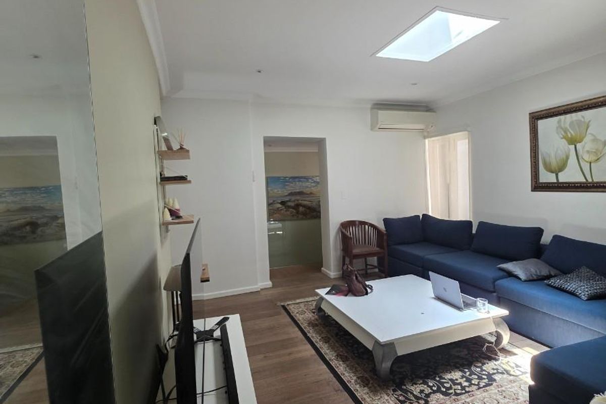 A well-lit living room featuring timber flooring, a skylight, and a wall-mounted air conditioning unit, offering a comfortable and functional living space.