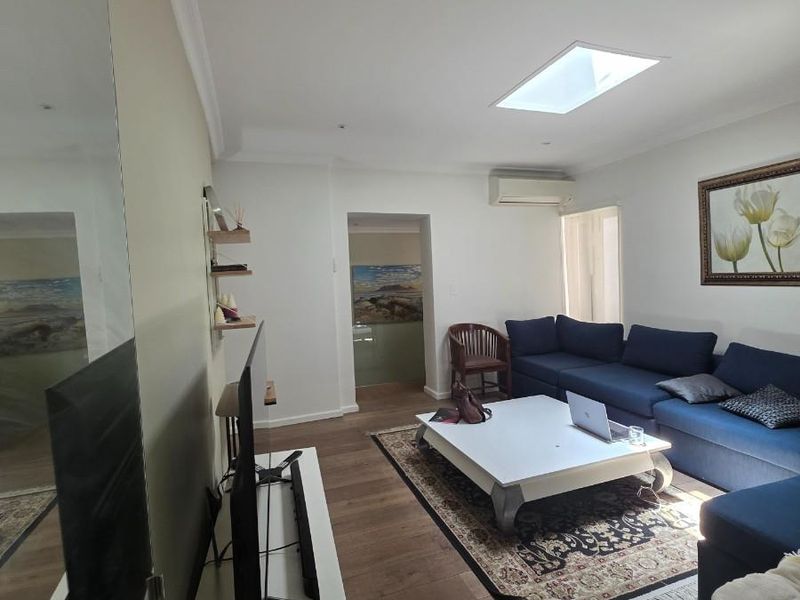 A well-lit living room featuring timber flooring, a skylight, and a wall-mounted air conditioning unit, offering a comfortable and functional living space.