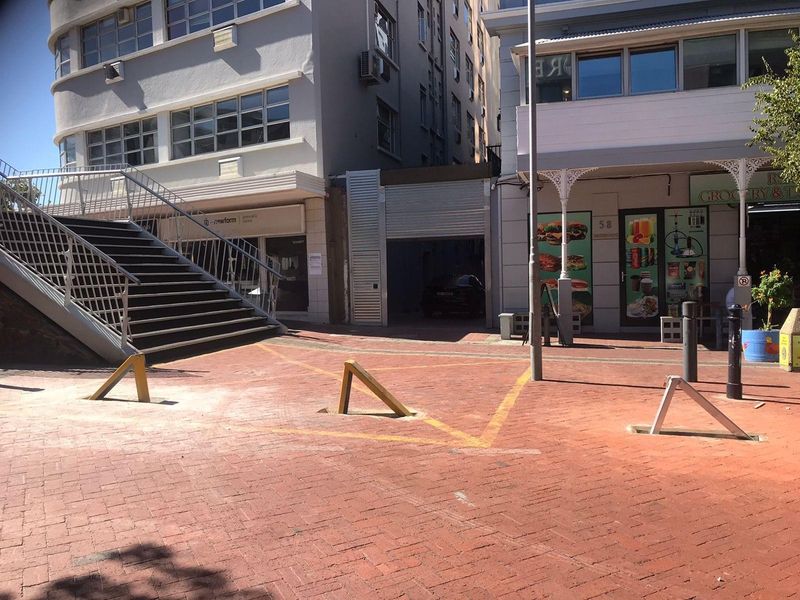Street-level view of an urban apartment building exterior featuring a paved walkway, metal staircase, and commercial storefronts at ground level.