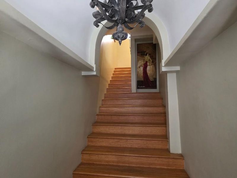 A well-maintained interior hallway featuring a timber staircase, an elegant arched entryway, and a decorative wrought iron chandelier.