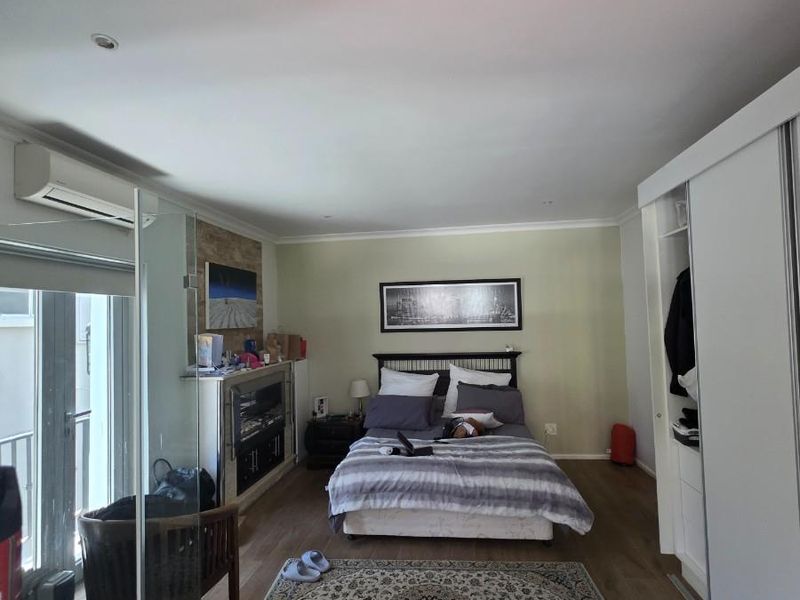Spacious bedroom featuring laminate flooring, built-in sliding door wardrobes, recessed lighting, and a wall-mounted air conditioning unit.