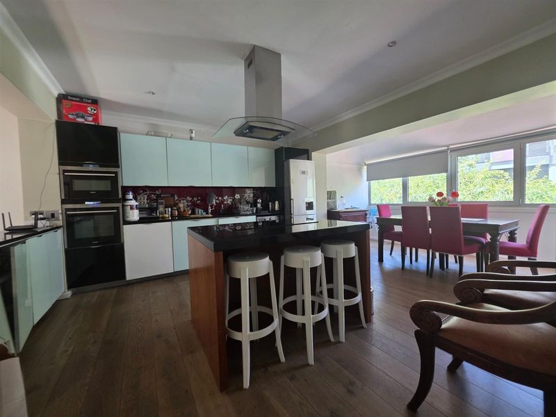 Open-plan kitchen and dining area featuring a central island, modern cabinetry, built-in appliances, and wood-look flooring with ample natural light.