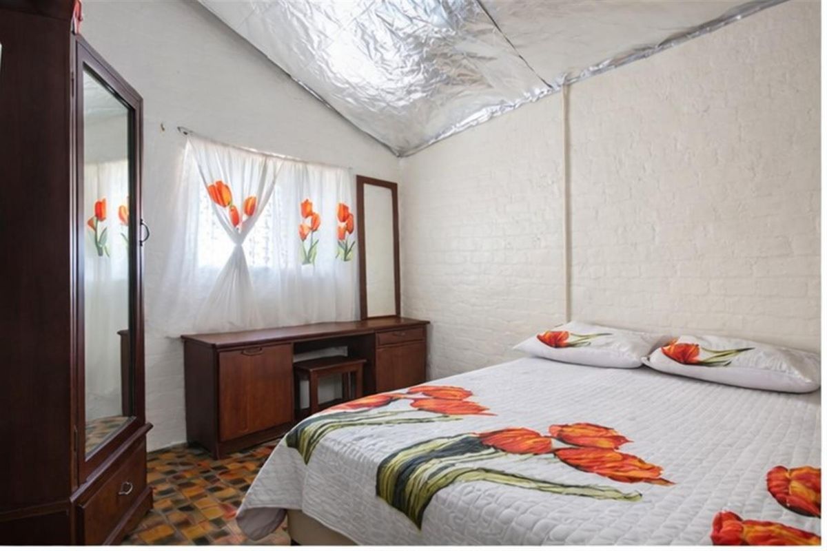 A bedroom featuring painted brick walls, a vaulted ceiling with exposed foil insulation, and tiled flooring.