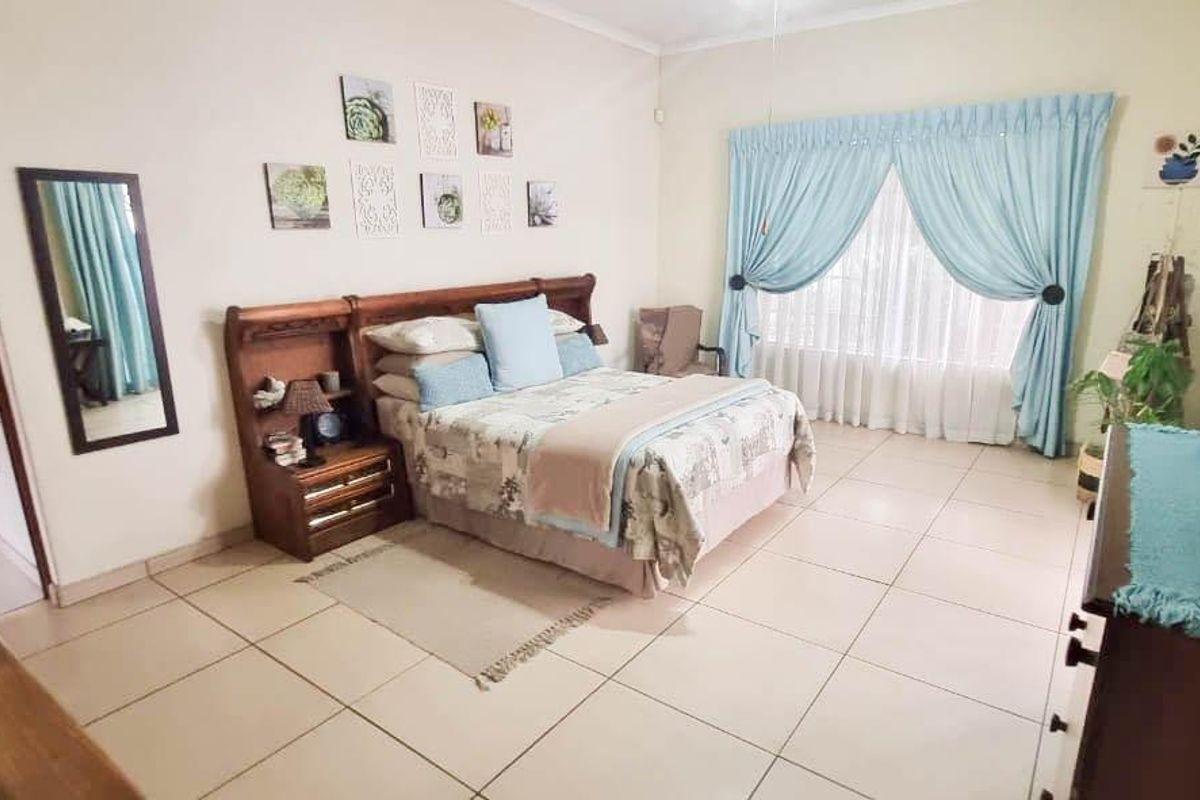 A spacious bedroom featuring neutral tiled flooring and large windows with curtains, providing a comfortable and well-lit living space.