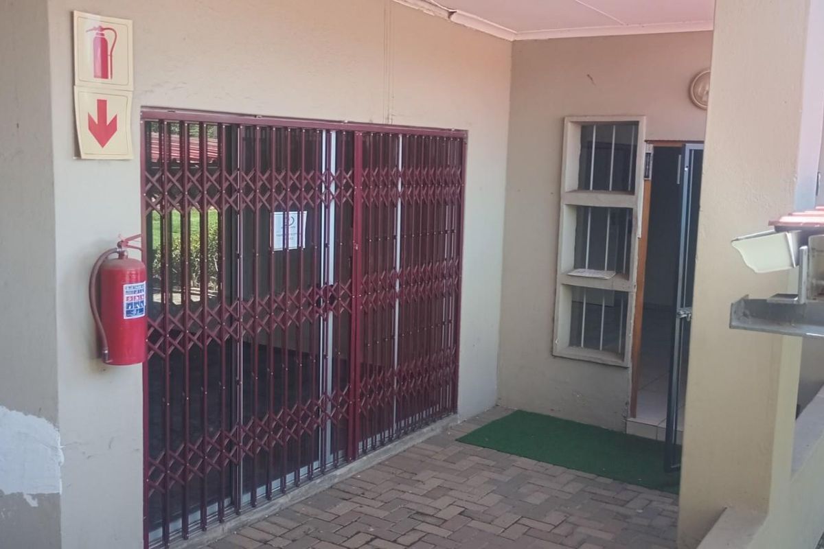 Rear exterior area of the office building featuring a security gate, fire safety equipment, and paved flooring with visible wall surface wear.