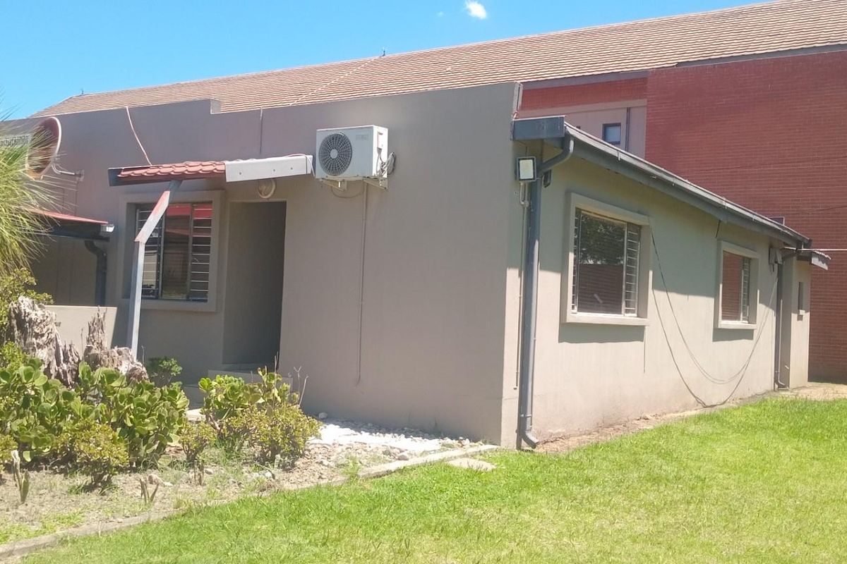 Rear exterior view of the office building featuring a tiled roof, security bars on windows, and an external air conditioning unit.