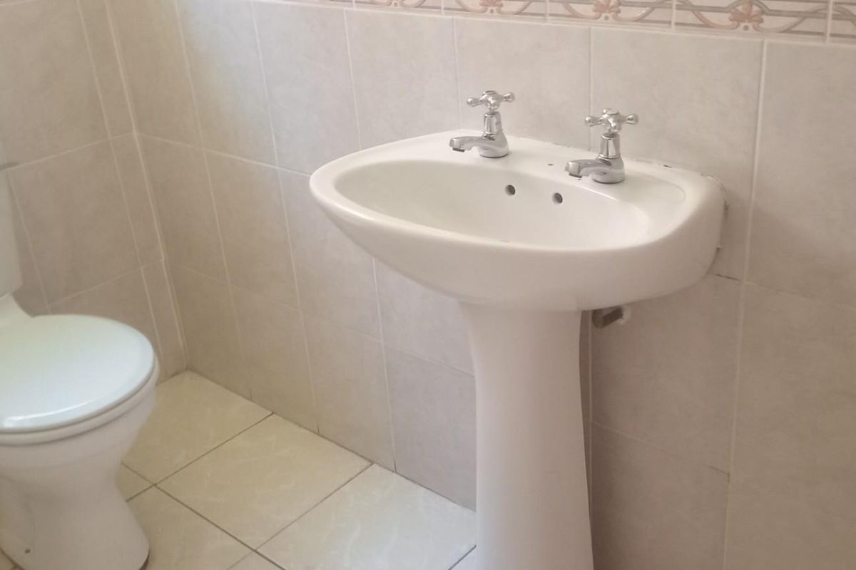 A functional bathroom featuring a pedestal basin and toilet with neutral ceramic wall and floor tiling.