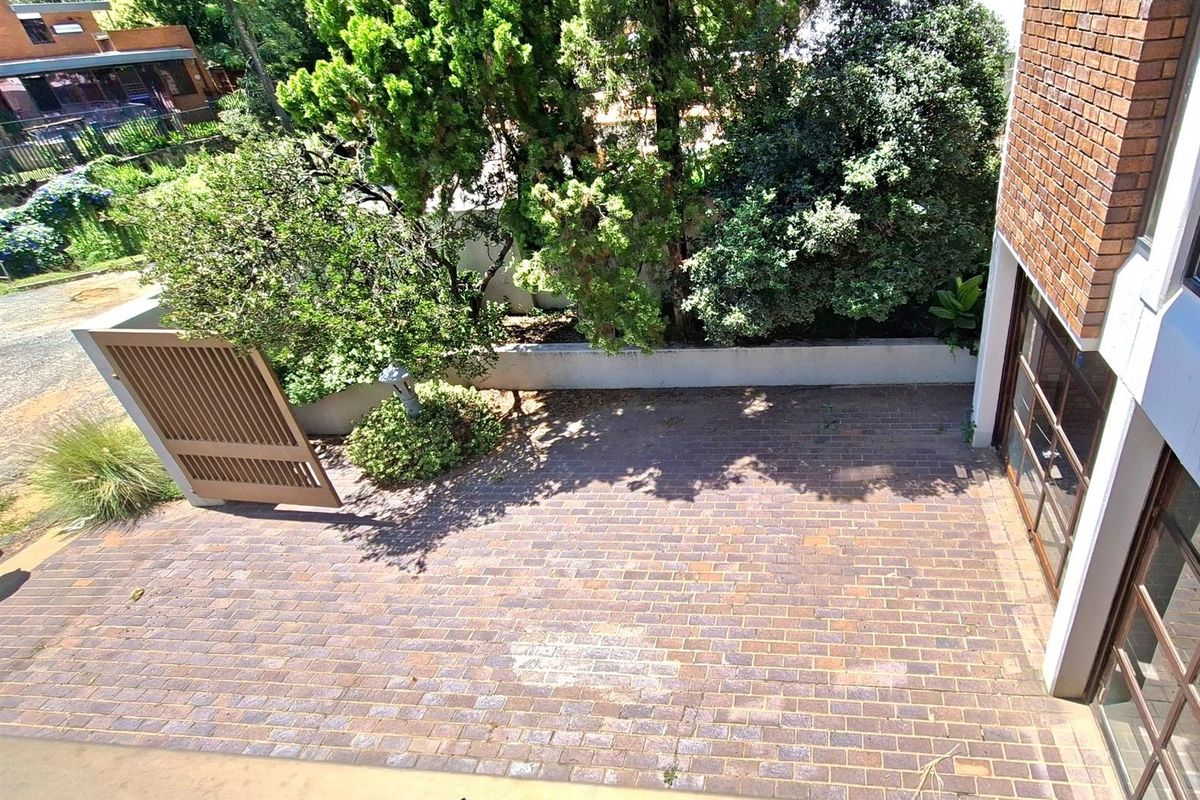 An elevated view of a private brick-paved courtyard area featuring mature trees, perimeter walls, and a gated entrance.