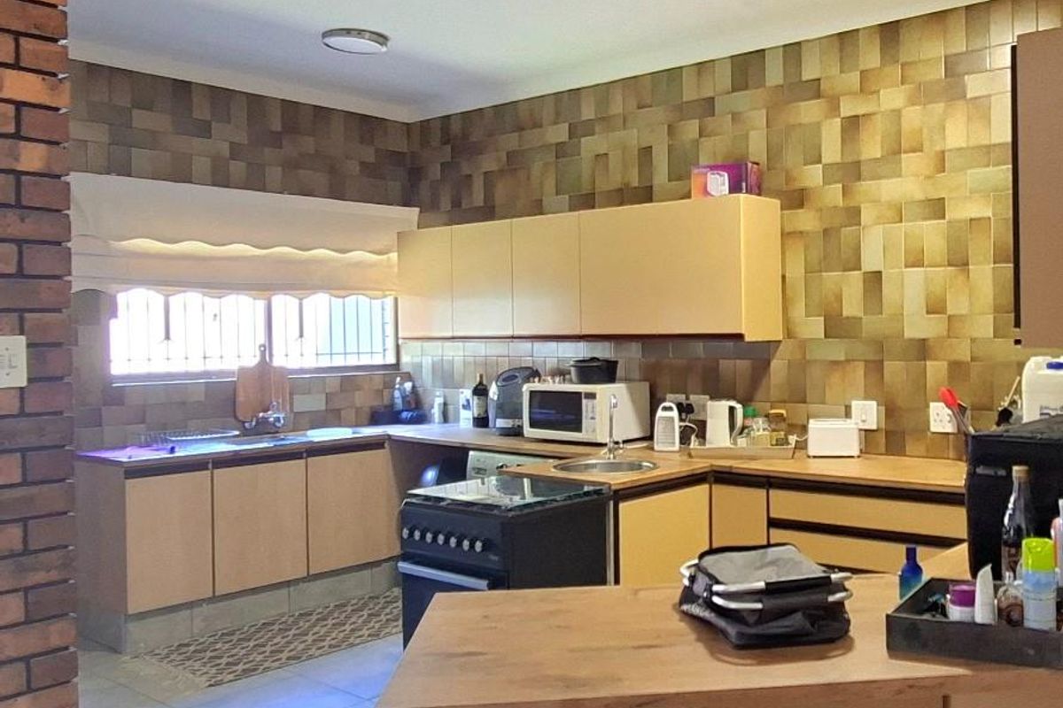 A functional kitchen featuring built-in cabinetry, a freestanding stove, and a breakfast bar, finished with textured wall tiles and tiled flooring.