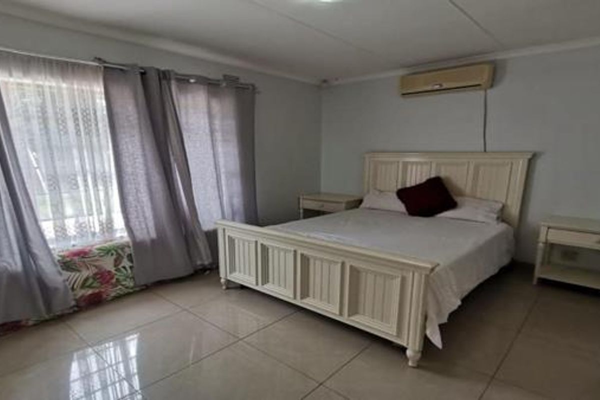 A spacious bedroom featuring tiled flooring, a wall-mounted air conditioning unit, and large windows with curtains.