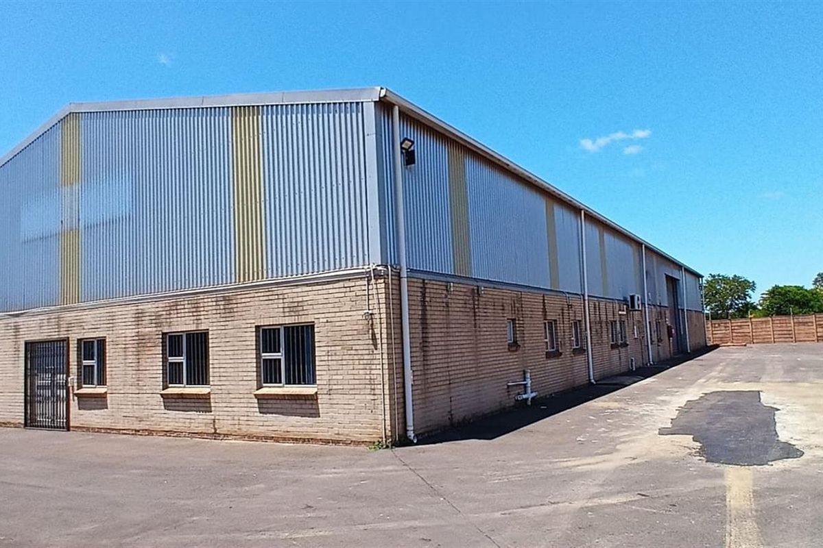 Industrial warehouse facility featuring brick and metal cladding construction, secure perimeter fencing, and an expansive paved yard area.