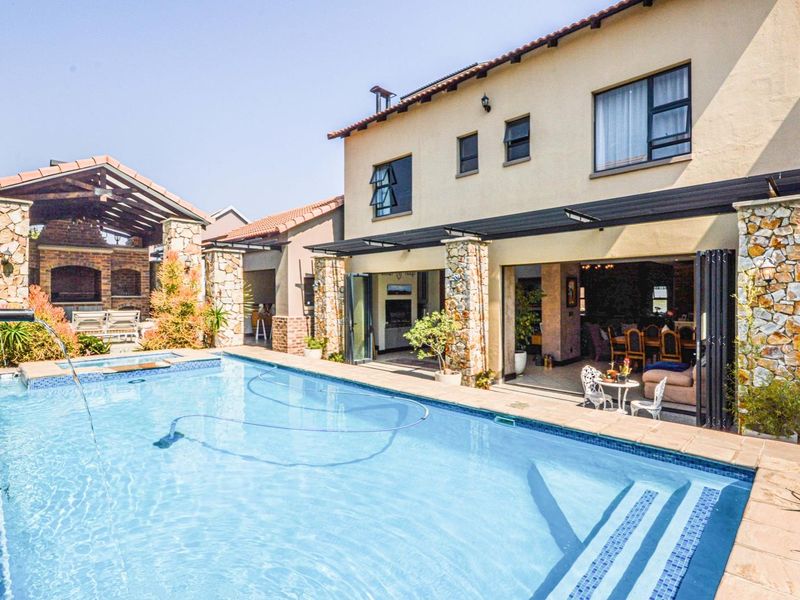 Spacious outdoor entertainment area featuring a swimming pool, covered patio with stacking doors, and a stone-clad built-in braai structure.