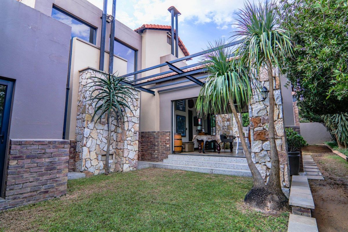 Rear exterior view featuring a stone-clad facade, metal pergola structure, and sliding glass doors leading to an indoor living space.