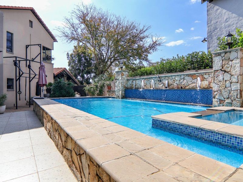 A well-maintained swimming pool area featuring stone-clad retaining walls, a decorative water feature, and tiled patio surrounds.