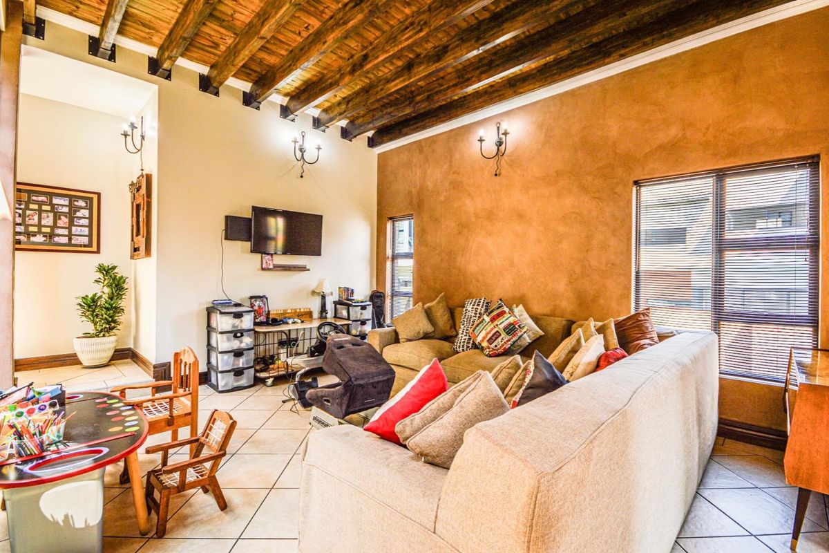 Spacious living room featuring exposed timber ceiling beams, tiled flooring, and warm-toned accent walls, offering a comfortable and character-filled living space.