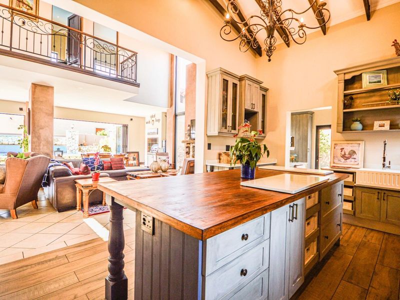 Spacious open-plan kitchen and living area featuring a large island, butler sink, exposed timber beams, and a mezzanine level with wrought iron detailing.