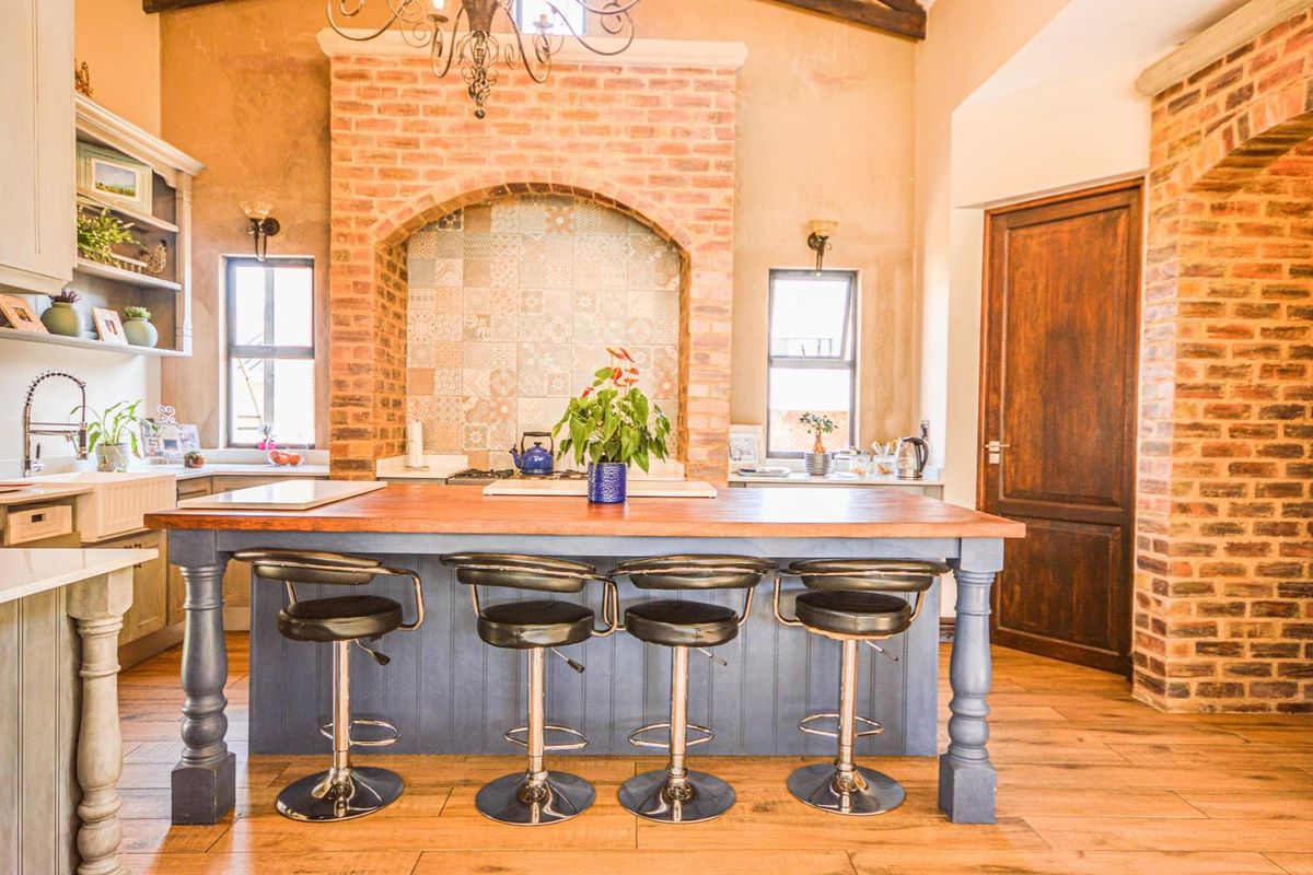 Spacious kitchen featuring a large central island with wooden countertop, exposed brick accents, vaulted ceilings, and farmhouse-style cabinetry.