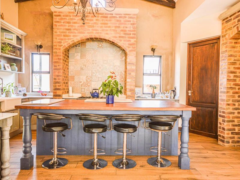 Spacious kitchen featuring a large central island with wooden countertop, exposed brick accents, vaulted ceilings, and farmhouse-style cabinetry.