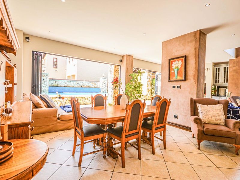 Spacious open-plan living and dining area featuring tiled floors, recessed lighting, and large stacking doors that open to an outdoor pool area.